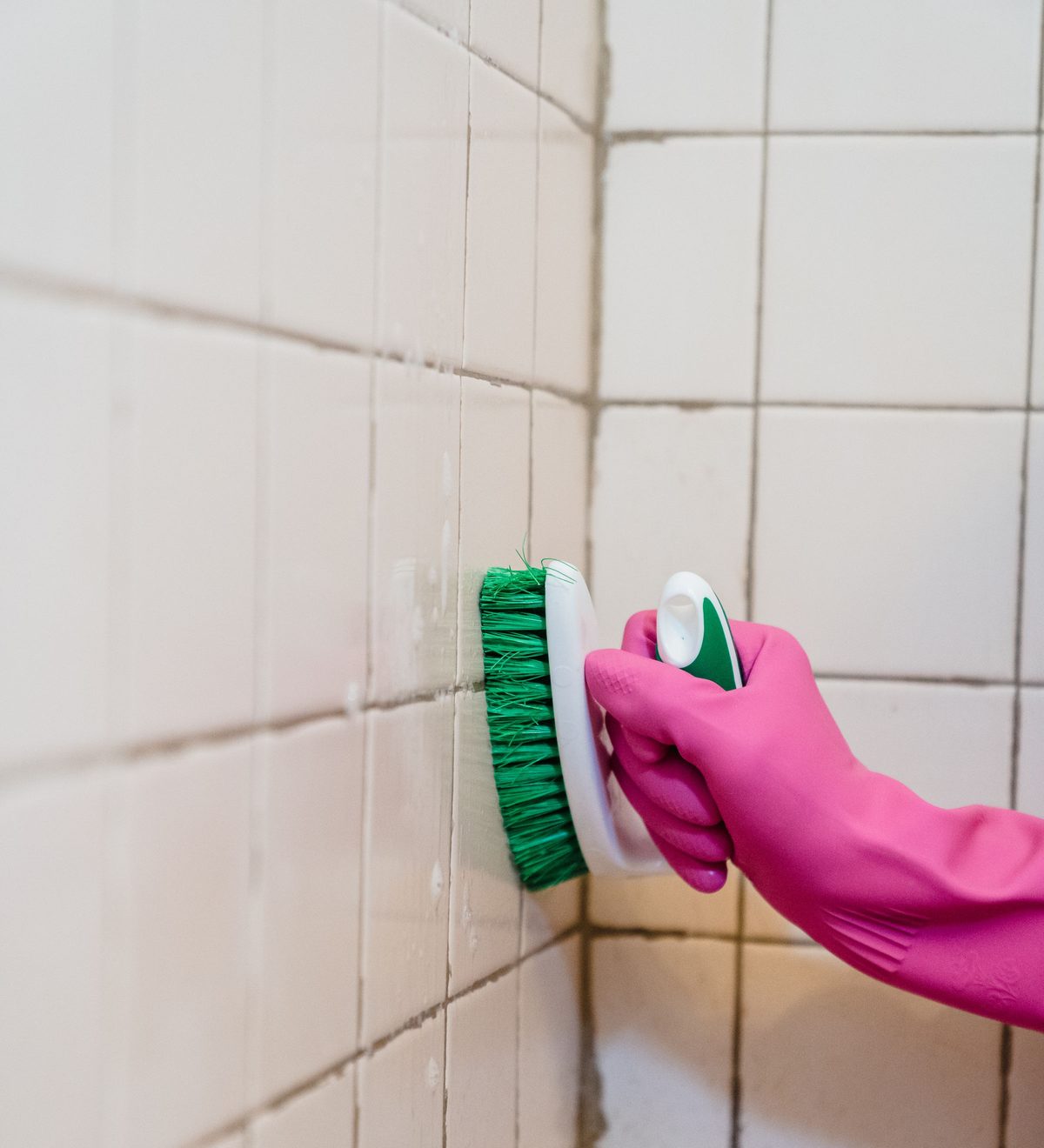 Eine Hand im Gummihandschuh schrubbt Badezimmerfliesen mit einer Bürste