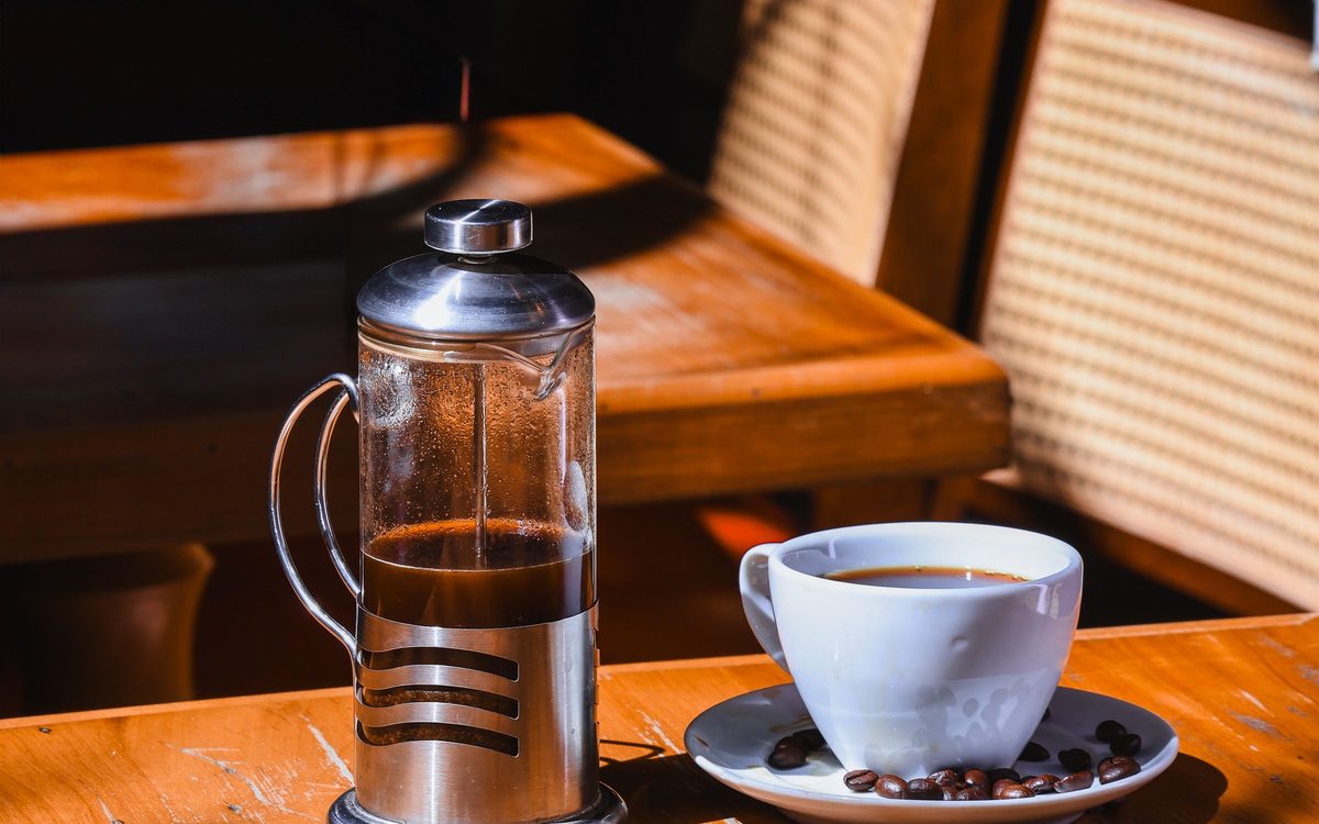 Eine French Press und eine Tasse Kaffee auf einem Holztisch im Sonnenlicht