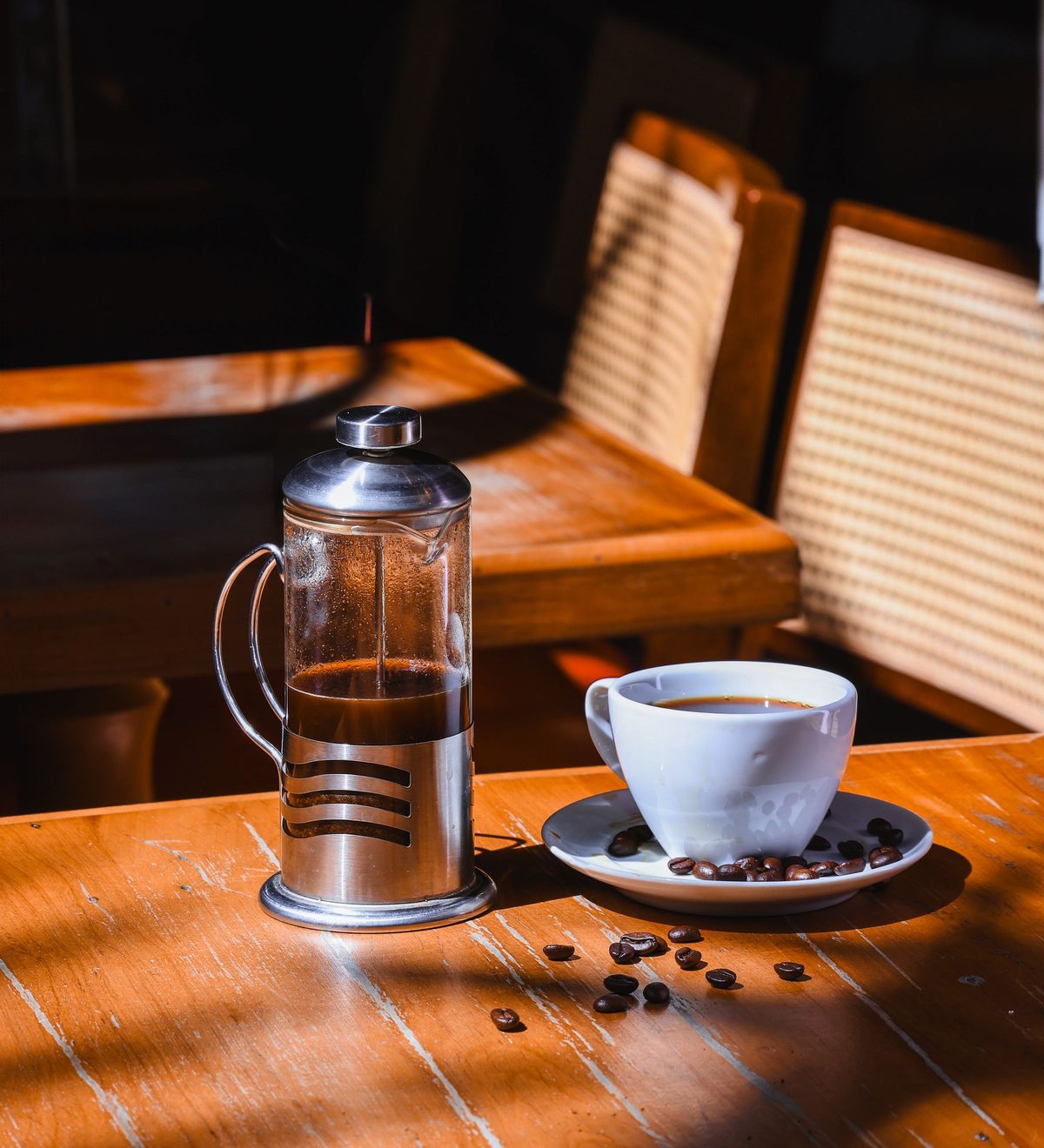 Eine French Press und eine Tasse Kaffee auf einem Holztisch im Sonnenlicht