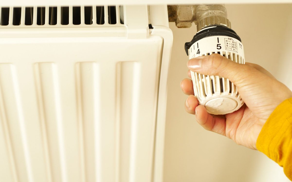 Hand dreht an einem Thermostatkopf an einem weißen Heizkörper