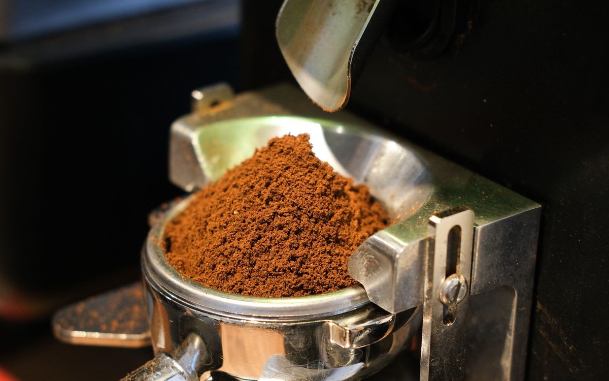 Frisch gemahlener Kaffee im Siebträger unter einer Kaffeemühle