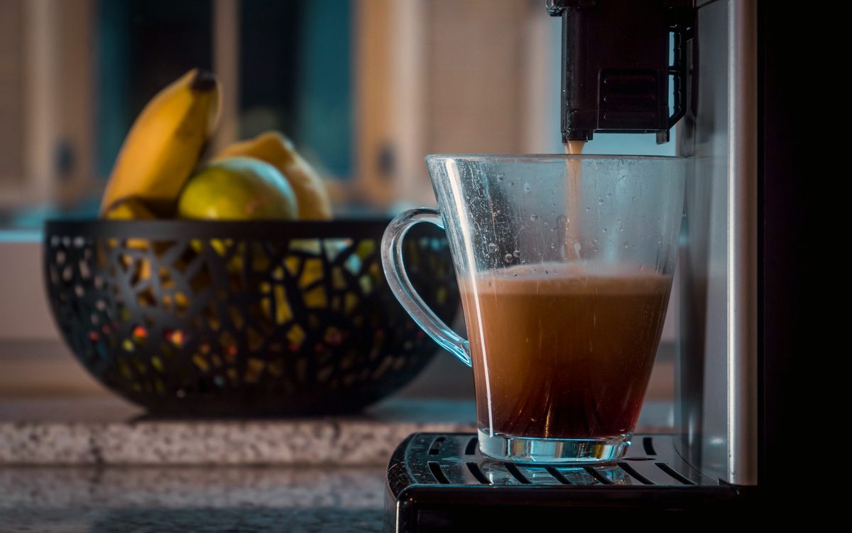 Kaffee läuft aus dem Auslauf eines Kaffeevollautomaten in ein Glas