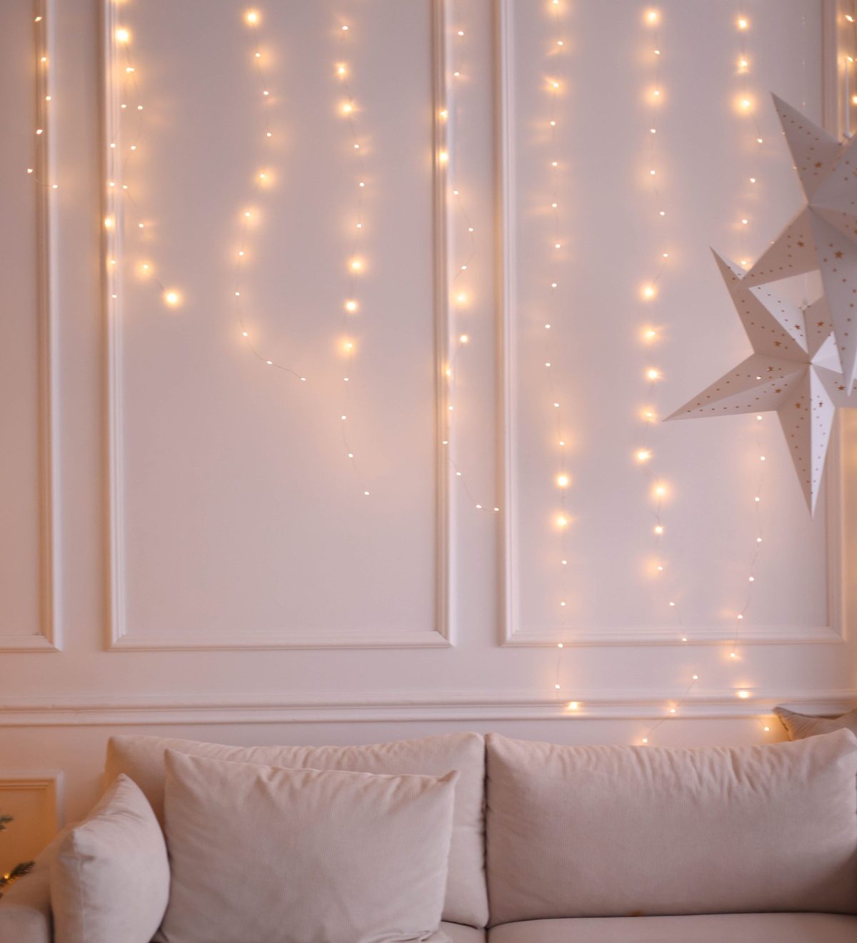Ein Lichtervorhang leuchtet warm hinter einem hellen Sofa