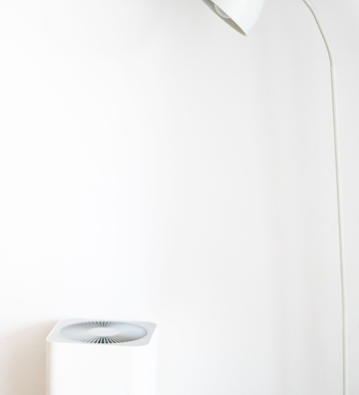 Weißer Luftreiniger neben einer Stehlampe in einem hellen, minimalistischen Raum