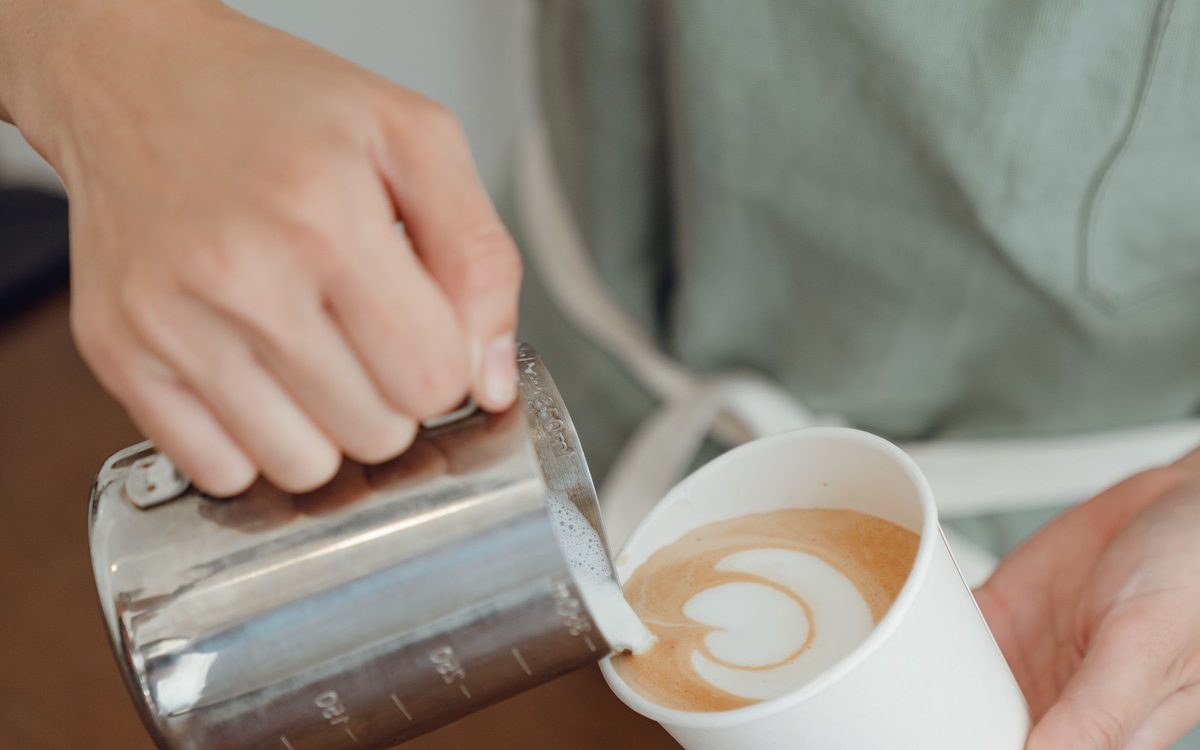 Milchschaum wird aus einem Kännchen in eine Tasse gegossen