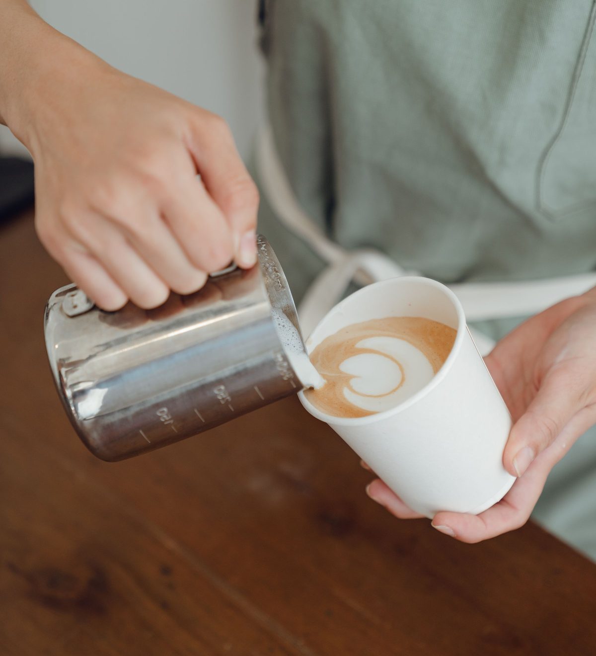 Milchschaum wird aus einem Kännchen in eine Tasse gegossen