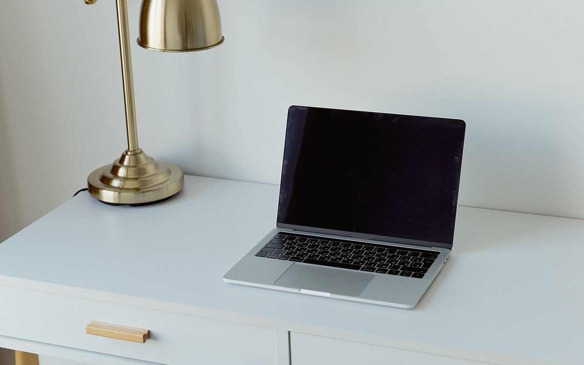 Heller Schreibtisch mit goldfarbener Schreibtischlampe und aufgeklapptem Laptop