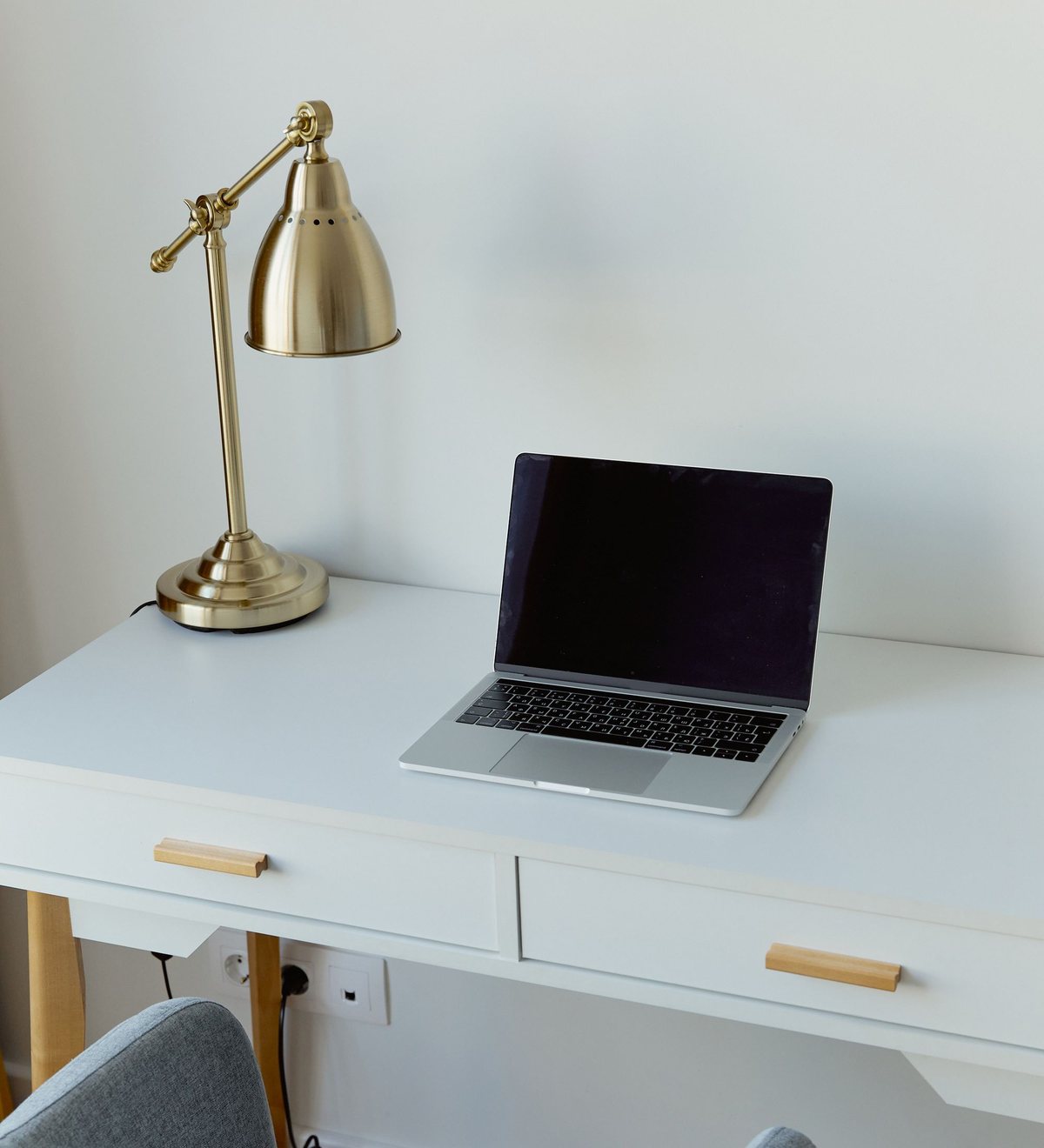Heller Schreibtisch mit goldfarbener Schreibtischlampe und aufgeklapptem Laptop