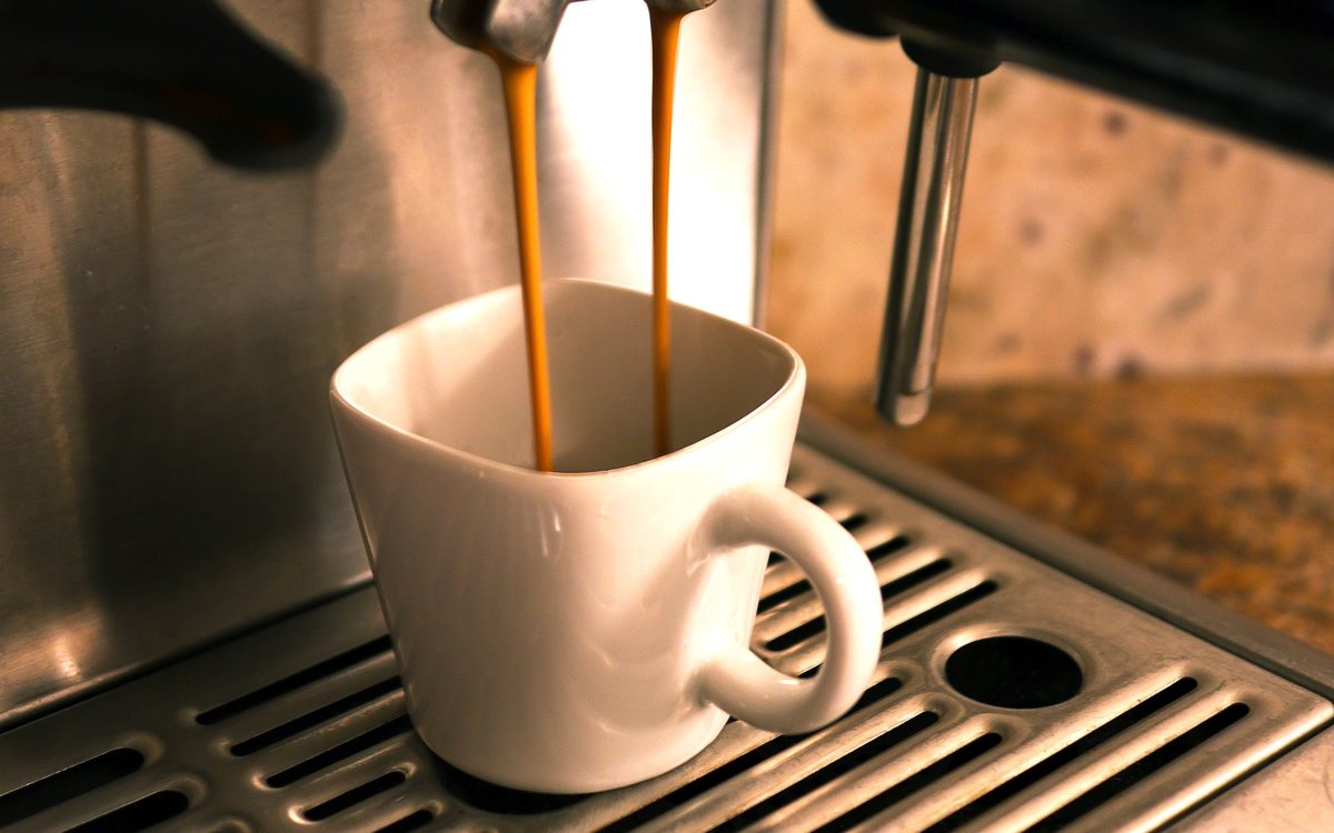 Espresso läuft aus einer Siebträgermaschine in eine weiße Tasse
