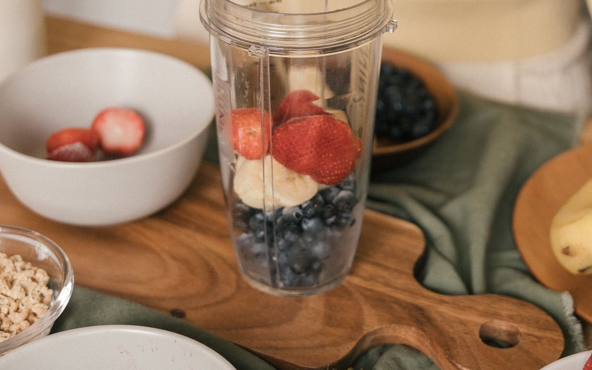 Beeren und Banane werden für einen Smoothie in einen Mixbecher gegeben