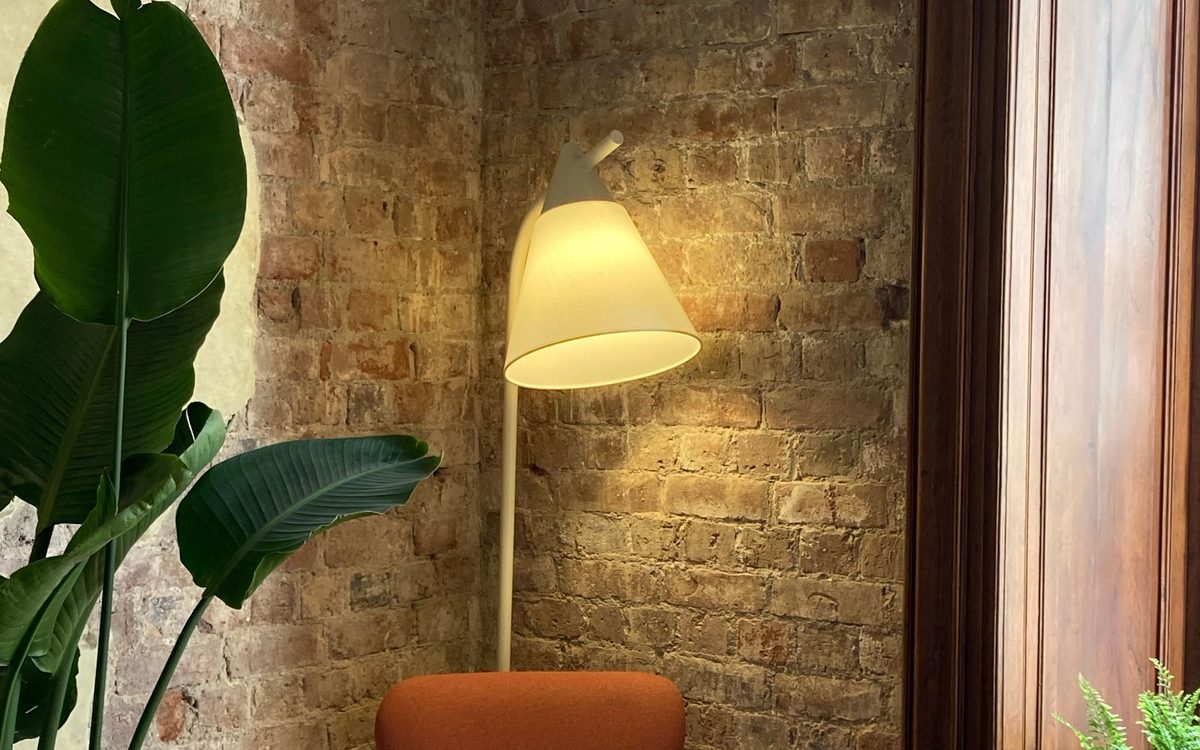 Leseecke mit rostrotem Sessel, Zimmerpflanze und warm leuchtender Stehlampe vor einer Ziegelwand