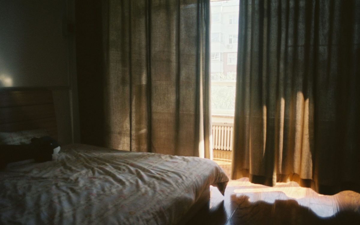 Morgenlicht fällt durch Vorhänge in ein dunkles Schlafzimmer