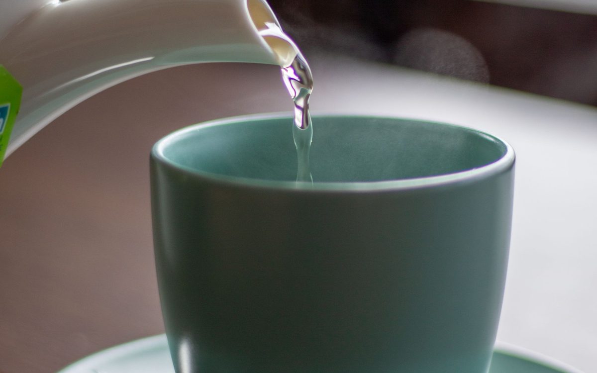 Heißes Wasser wird aus einem weißen Kocher in eine türkisfarbene Tasse gegossen