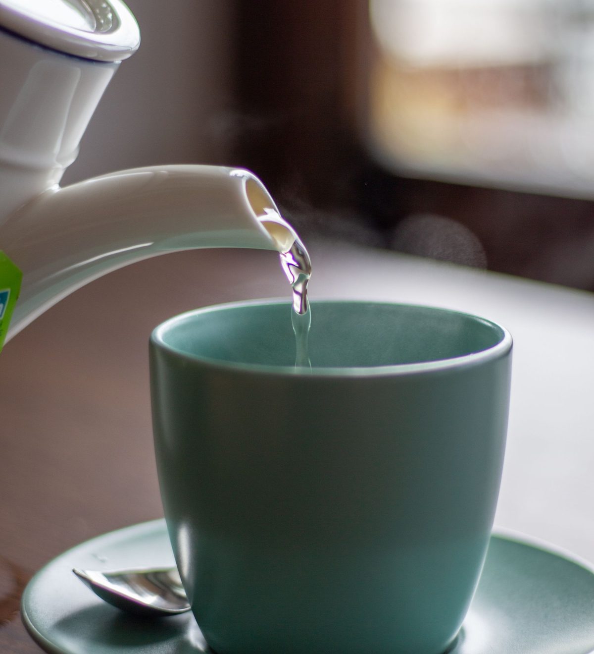 Heißes Wasser wird aus einem weißen Kocher in eine türkisfarbene Tasse gegossen