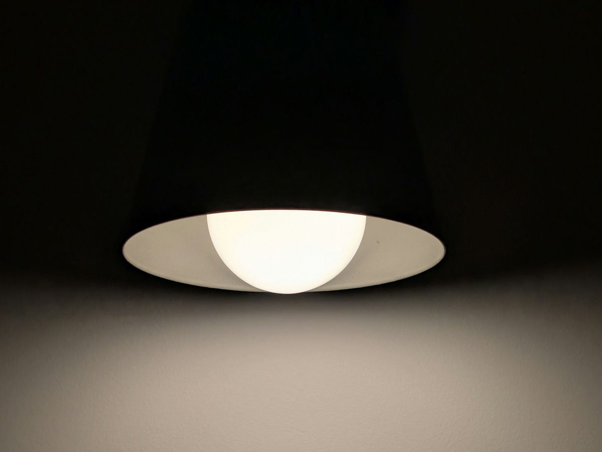 Moderne Pendelleuchte mit warm leuchtender LED-Lampe vor dunklem Hintergrund